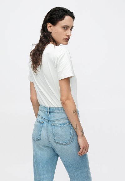 Λευκό κοντομάνικο μπλουζάκι συνδυασμένο με ανοιχτό μπλε ψηλόμεσο τζιν, με δύο πίσω τσέπες και χαλαρή εφαρμογή. Ομαλή υφή.