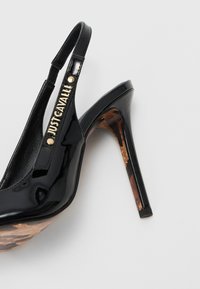 Scarpa con tacco alto in pelle verniciata nera, con cinturino slingback e un tacco a trama marrone e nero. Dettaglio di branding dorato incluso.