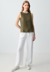 Top senza maniche verde oliva in lino, abbinato a pantaloni larghi bianchi in lino. Il modello indossa delle sneaker bianche. Design minimalista, texture naturali.