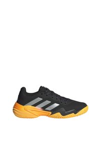 Černá sportovní bota se stříbrnými pruhy, oranžovými akcenty na patě, texturovaným síťovaným svrškem a vzorovanou gumovou podrážkou pro lepší přilnavost.