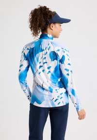 Långärmad skjorta med blå abstrakt mönster på vit tyg, med krage och rundad nederkant, ihopparad med marinblå byxor.