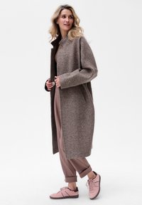 Bruin visgraatjack met een brede kraag, gedragen over een beige top en bruine broek. Gepaard met lichtroze sneakers met donkere accenten.
