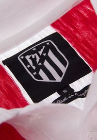 Wit stoffen label met zwart logo van een schild met strepen en sterren, omringd door rode stof, gemarkeerd met "Gemaakt in Europa" en maat "S."