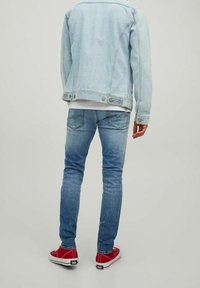 Ljusblå denimjacka, mellanblå tajta jeans och röda sneakers, sett bakifrån. Jackan har sömmar och klassiska knappar.