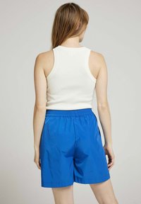 Débardeur blanc côtelé associé à un short bleu léger avec taille élastique. Le short a une texture lisse et une coupe ample et décontractée.