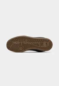 Solea de cauciuc maro a unei pantofi negri cu modele de tread hexagonale și liniare și un design circular aproape de minge.