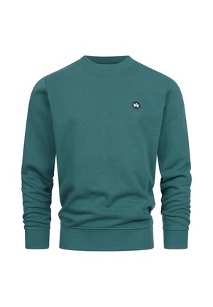 Turkos bomullströja med långa ärmar, rund halsringning och ribbade muddar och nederkant. Har en liten svart logotyp på bröstet.