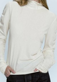 Weißes Langarm-Turtleneck-Shirt aus leichtem Stoff, mit enganliegender Passform und gerippten Akzenten an den Bündchen und am Kragen.
