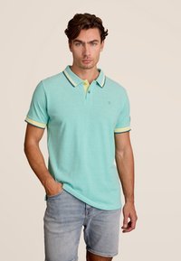 Lichtblauwe polo met een gele en marineblauwe gestreepte kraag, korte mouwen met bijpassende accenten, gemaakt van een zachte, gestructureerde stof.