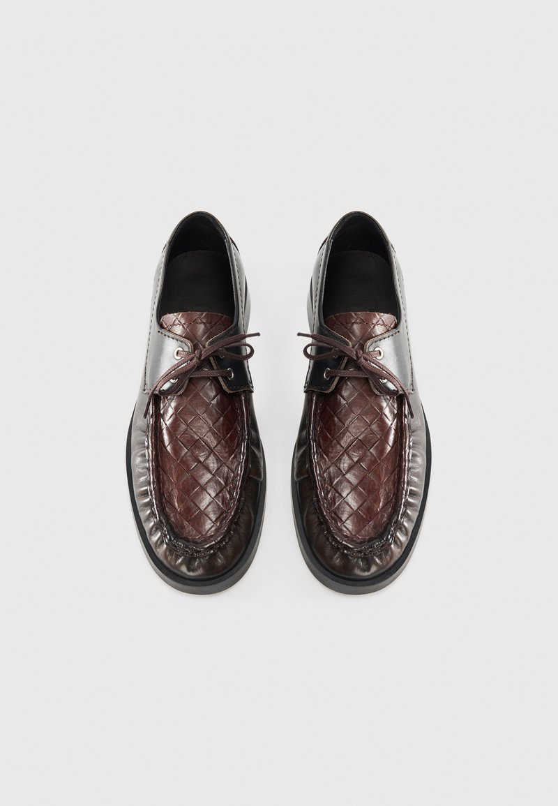 Chaussures en cuir tissées marron avec un bout poli marron foncé, lacets ronds et une forme arrondie. Accents noirs lisses au niveau du col.
