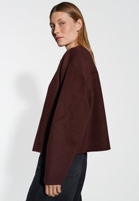 Burgundy oversized wool blend sweater with a cropped hem, dropped shoulders, and minimalistic design, paired with dark jeans.