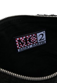 Interno nero di una borsa con un'etichetta logo. L'etichetta presenta un motivo a scacchi rosso e bianco con la scritta "MC2 SAINT BARTH" in caratteri grassetto.
