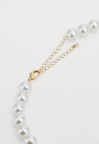 Collier en perles comprenant cinq perles blanches rondes et brillantes, reliées par une chaîne en or et un fermoir, offrant une fermeture sécurisée.