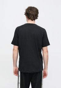 Μαύρο βαμβακερό κοντομάνικο μπλουζάκι με χαλαρή εφαρμογή, με μανίκια ράγκλαν και ομαλή υφή, απεικονίζεται από πίσω πλευρά.