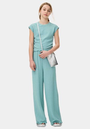 Completo coordinato di due pezzi in un blu chiaro strutturato, composto da una maglietta a maniche corte e pantaloni a gamba larga, abbinato a una piccola borsa a tracolla in argento.