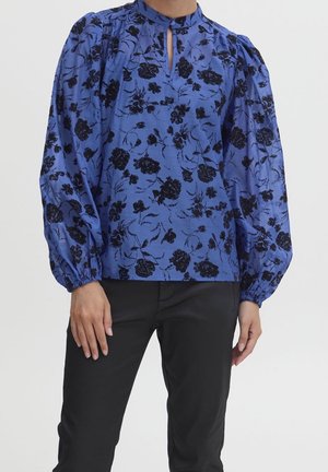 Blaue Bluse mit floralem Muster in Schwarz, mit gepufften Ärmeln, Keyhole-Ausschnitt und glatter Textur; kombiniert mit schwarzen Hosen.