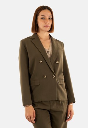 Blazer verde oliva de doble botonadura con botones metálicos, solapas de muesca y bolsillos laterales, combinado con una blusa clara de escote en v y pantalones a juego.