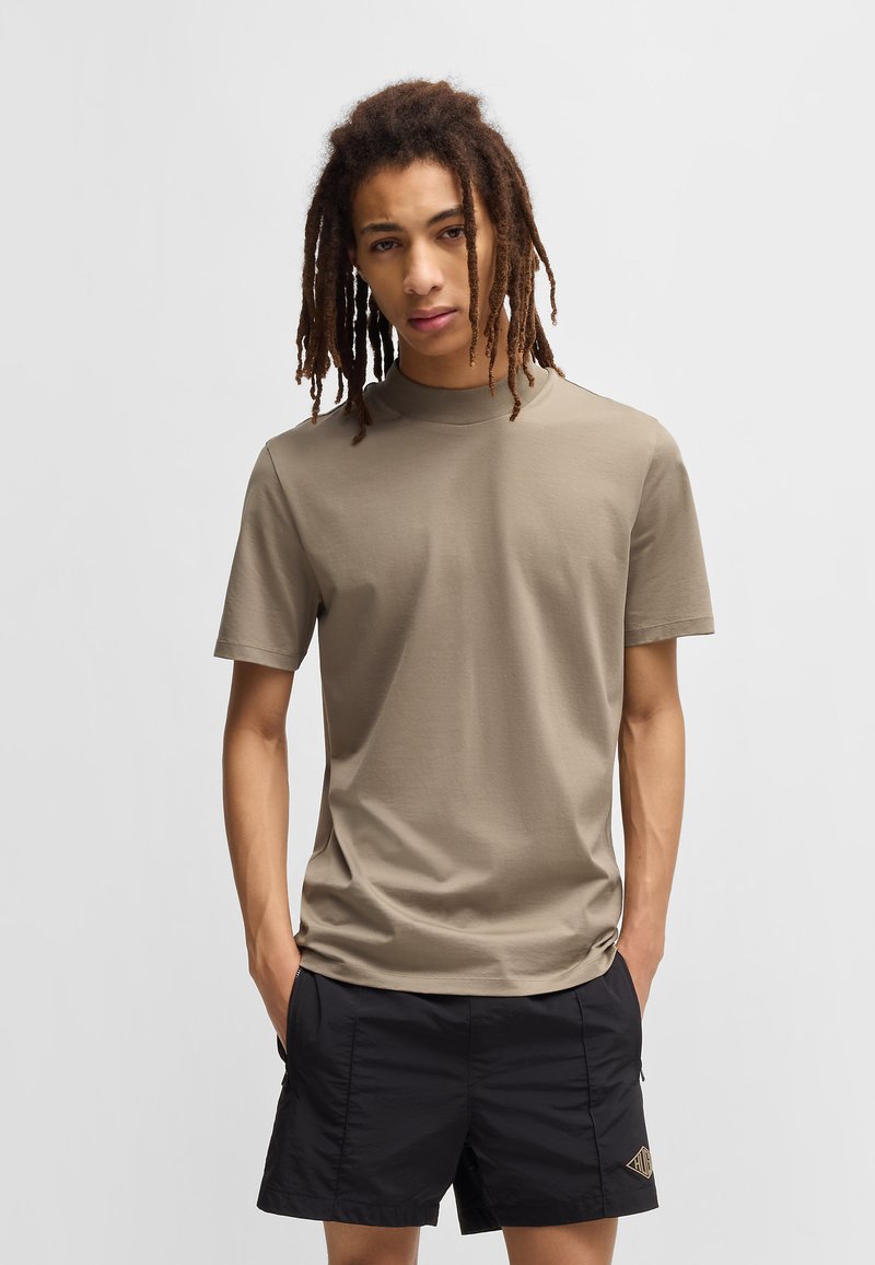T-shirt khaki a maniche corte realizzato in tessuto morbido, caratterizzato da un collo alto e una vestibilità ampia. Abbinato a pantaloni corti neri con un logo sottile.