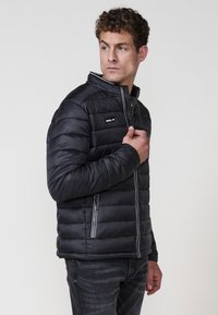 Crna puffer jakna s uzdignutim ovratnikom, bočnim džepovima na zip, i horizontalnim šavovima. Glatka tekstura s elegantnim dizajnom.