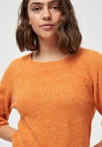 Maglione lavorato a maglia di un vibrante arancione, con una superficie texturizzata, scollatura rotonda e maniche a tre quarti. Materiale morbido e accogliente.
