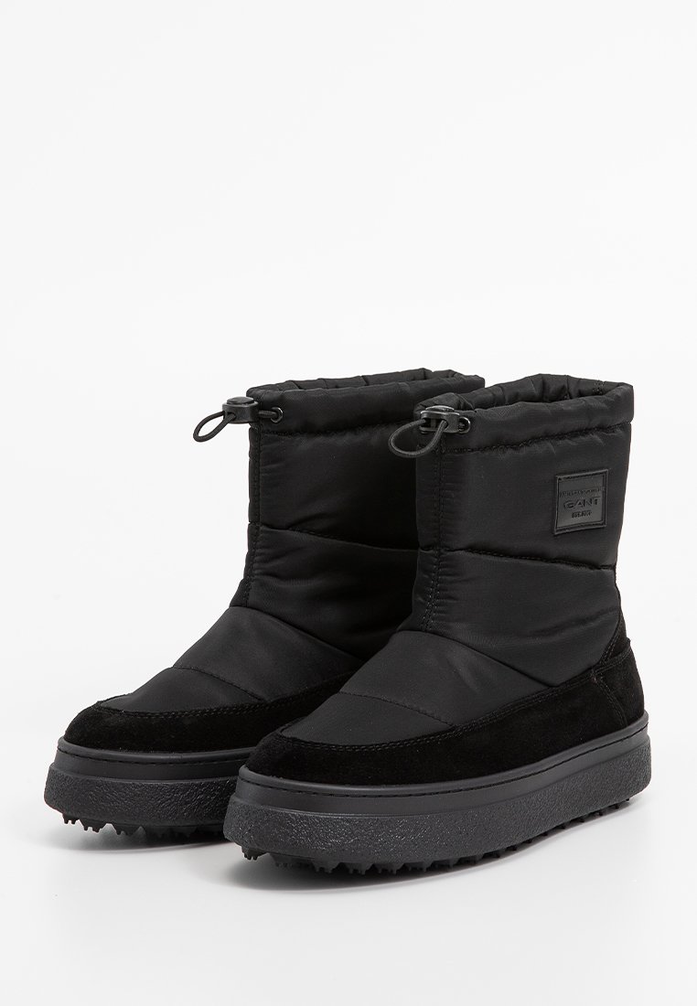 Botas de invierno negras con parte superior acolchada, acentos de ante y suelas de goma texturizadas. Cuenta con cierre de cordón elástico y un parche con logo en el lateral.