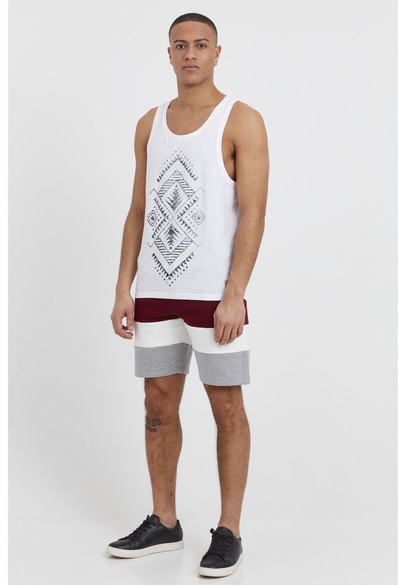 Hvid tanktop med sort geometrisk print, parret med bordeaux, hvid og grå stribede shorts. Sorte sneakers fuldender outfittet.