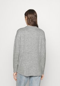 Pull en tricot texturé gris avec un col rond, des épaules tombantes et une coupe décontractée, présentant un ourlet arrière légèrement plus long.