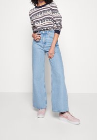 Jeans de pierna ancha color azul claro combinados con un suéter de punto estampado y zapatillas rosas. El conjunto presenta un diseño casual y en capas.