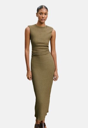 Olivengrünes, figurbetontes Midi-Kleid mit kurzen Ärmeln, strukturiertem Stoff und Raffung am Taillenbereich, kombiniert mit dunkelbraunen Blockabsätzen.