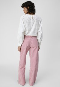 Blouse blanche en dentelle avec des manches bouffantes et un petit trou au dos, associée à un pantalon large à rayures rouges et blanches à taille haute. Texture lisse.