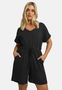 Svart kortärmad jumpsuit i mjukt tyg, med v-ringning, elastisk midja och sidfickor för funktionalitet.