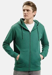 Zielona bluza z zamkiem błyskawicznym, z kapturem ze sznurkiem, z kieszeniami z przodu i miękką strukturą. Wykonana z mieszanki bawełny, posiada ściągacze na rękawach i u dołu.