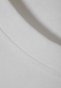 White cotton fabric with a ribbed neckline, featuring flatlock stitching along the edge, showcasing a smooth and soft texture.