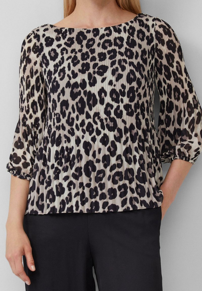 Blouse à imprimé léopard avec manches trois-quarts, tissu plissé, encolure arrondie et coupe décontractée, associée à un pantalon noir.