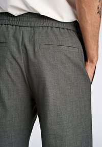 Grijze broek met elastische taille en een gestructureerde afwerking. Voorzien van twee achterzakken en gestikte details. Minimalistisch ontwerp.