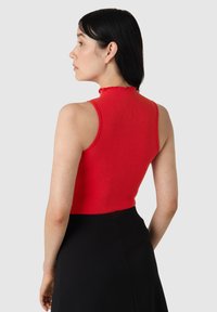 Top rosso a coste senza maniche con colletto scallop, abbinato a una gonna nera. Il top presenta un design aderente e una texture liscia.