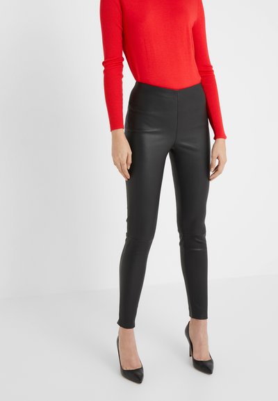 Leggings en similibois noirs avec taille haute et coupe ajustée, accompagnés d'un top rouge à manches longues et de talons noirs à bout pointu.