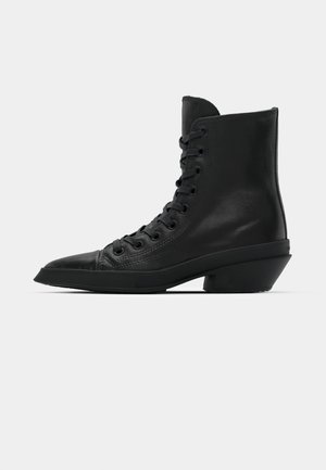Bottines en cuir noir avec un bout pointu, un devant à lacets plat et un design de talon bloc unique. Texture lisse et style minimaliste.