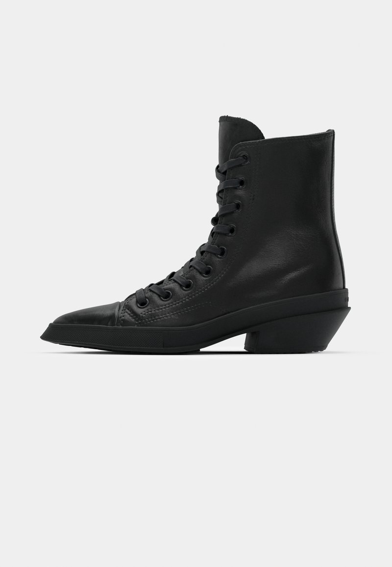 Bottines en cuir noir avec un bout pointu, un devant à lacets plat et un design de talon bloc unique. Texture lisse et style minimaliste.