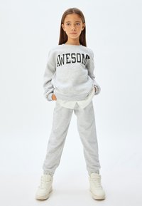 Sudadera gris claro con la palabra "AWESOME" en texto negro, combinada con pantalones de chándal a juego. El conjunto presenta un corte relajado y puños elásticos.