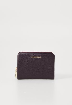Compact dark purple leather wallet with gold zipper and "Coccinelle" logo embossed in gold on front center.