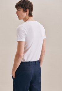 T-shirt bianco in cotone abbinato a pantaloni eleganti blu. Il T-shirt ha un collo rotondo e maniche corte; i pantaloni presentano tasche laterali e cuciture sul retro.