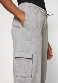 Grå mjukisbyxor tillverkade av mjukt tyg, med elastisk midja och dragsko, sidfickor och en ficka i cargo-stil.