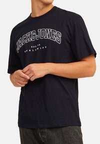 Navy blue cotton t-shirt with short sleeves, featuring a white graphic print "JACK&JONES" and text "EST.90 WORLDWIDE" on the front.