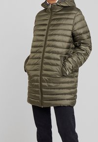 Olivově zelená péřová bunda s horizontálním prošíváním, plný zip, dvě boční kapsy a kapuce. Vyrobena z lesklého, lehkého materiálu.