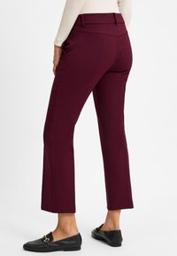 Bordeauxkleurige tailored broek met een slim fit, met een hoge taille, voorzakken en een soepele stoftextuur. Zwarte loafers gedragen bij de broek.