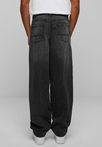 Dark gray wide-leg jeans made of denim, featuring a high waist, two back pockets, and a relaxed fit. Pairing with white sneakers.