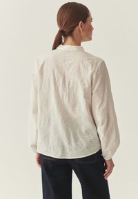 Blouse blanche avec motifs de feuilles brodés, manches longues et ourlet arrondi. Confectionnée dans un tissu léger à la texture douce.