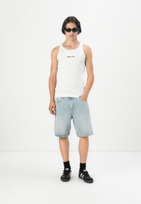 Hvitt ribbet tanktop med svart logo, lyseblå denimshorts, svarte joggesko med hvite striper, og solbriller. Minimalistisk design.