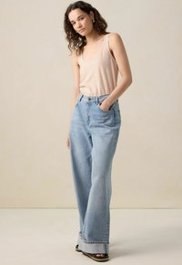 Débardeur léger rayé dans les tons pêche et blanc, associé à un jeans en denim bleu clair taille haute et à jambes larges, avec un ourlet brut.